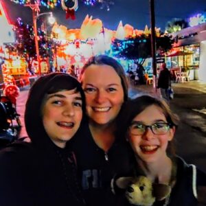 Erin and her two kids smiling in a selfie taken on a colorful street at night